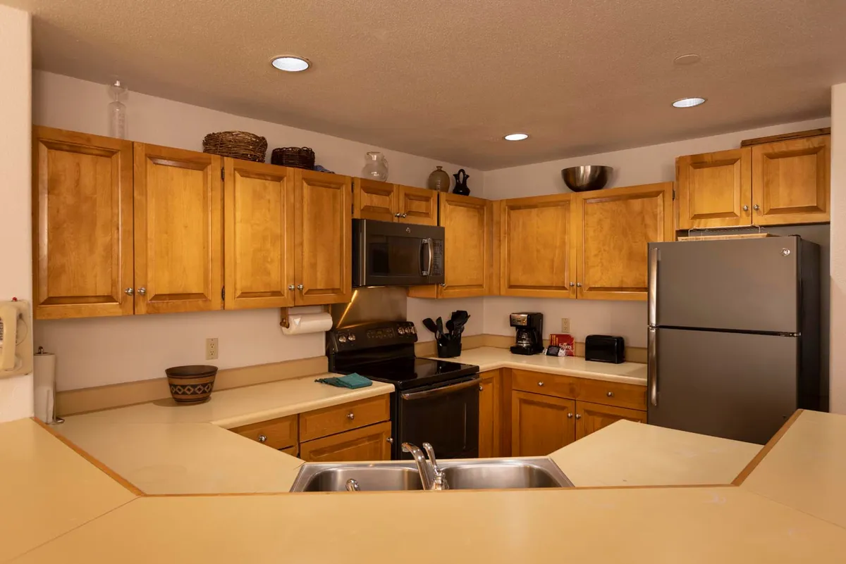 A close-up view of wooden cabinetry, stainless steel appliances, double sink, and ample counter space. The setup is practical for meal preparation and gathering, with a warm and inviting ambiance that encourages casual conversation and teamwork in the kitchen.